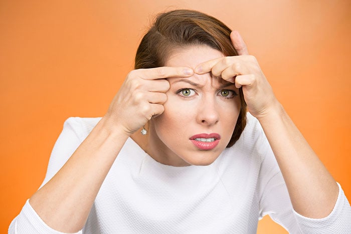 Closeup portrait, young pretty beautiful frustrated woman surprised stunned to see zit on her face, isolated orange background. Negative emotion facial expression feelings, situation, reaction-1