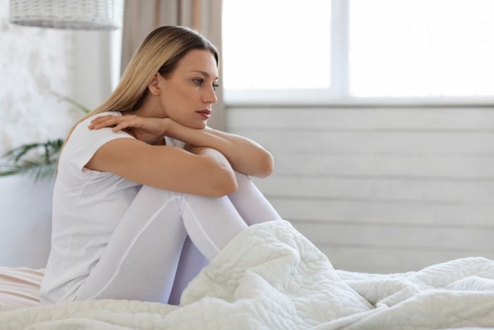 pensive-young-woman-sitting-on-bed-alone