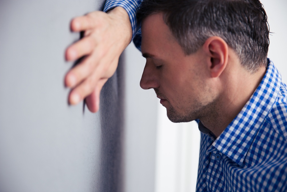 Stressed man with closed eyes leaning on the gray wall